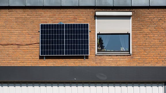 Solarpaneel und Kabel an einer Hauswand neben einem Fenster eines Wohnhauses