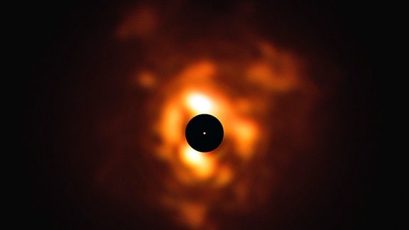 In der Mitte verdeckt eine schwarze Scheibe die direkte Nachbarschaft des Sterns, damit sein Umfeld nicht überstrahlt wird. In der Mitte ist der rote Überriese zu sehen.