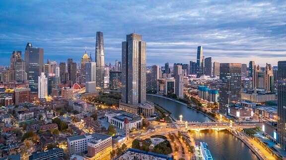 Großstadt Tianjin in Dämmerung mit Abendsonne und glänzenden Hochhausfassaden an Fluss