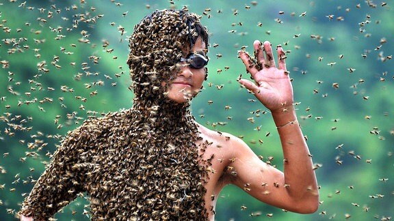Der Körper eines jungen Mannes ist fast vollständig mit Bienen bedeckt