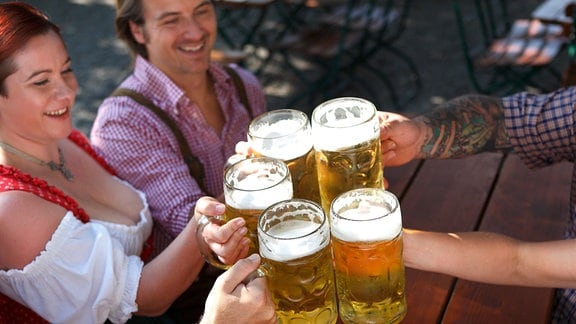 Ansicht von schräg oben: Männer und Frauen in traditioneller bayerischer Kleidung stoßen mit Maßkrügen voll Bier an.
