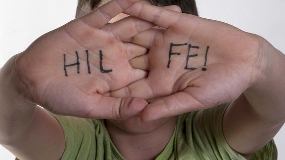 Ein Junge zeigt seine Handinnenflächen auf denen das Wort Hilfe steht