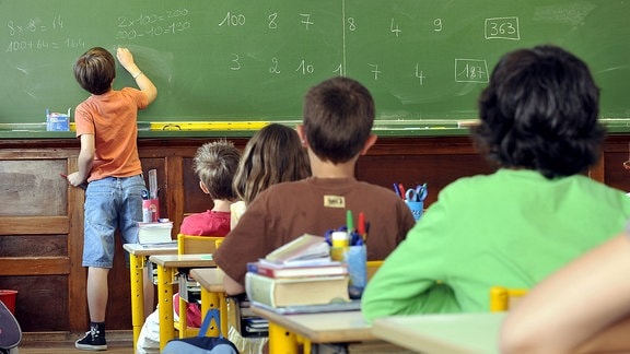 Ein Junge schreibt im Klassenzimmer an die Tafel.