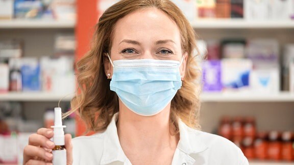 Apothekerin trägt medizinische Maske und hält Nasenspray in der Hand