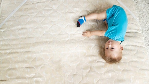 Ein Kind liegt auf einer Matratze.