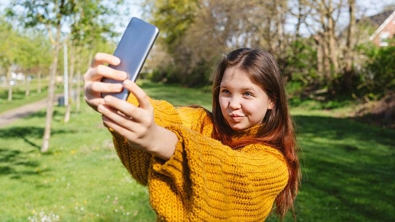 Lächelndes Mädchen, das im Park ein Selfie mit dem Smartphone macht.