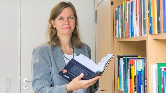 Professor Tinka Reichmann blättert neben einem Regal in einem dicken Buch 