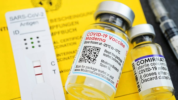 Impfausweis mit Impfspritze, positivem Corona-Schnelltest und Impfstofffläschchen von Biontech und Moderna
