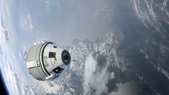Das Starliner-Raumschiff von Boeing im Weltraum. Im Hintergrund erkennt man die Erde.