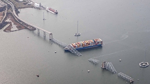 Brücke aus der Luft, mittlers Teil in Wasser gestürzt, daneben großes Containerschiff