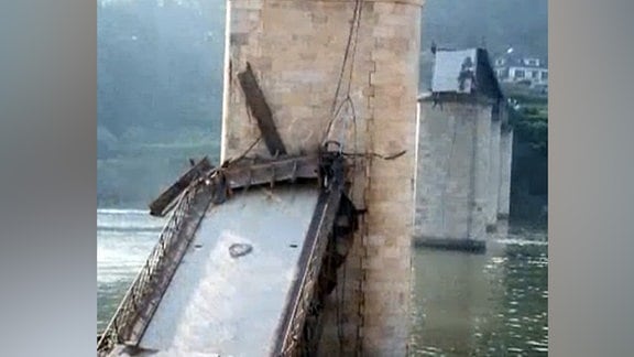 Nahaufnahme herabgestürzte Brückendecke an Brückenpfeiler in Fluss, dahinter weitere Pfeiler, teilweise mit noch vorhandener Decke