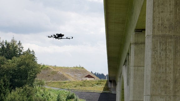 Fotodrohne fliegt neben Brückenpfeiler von Brücke über Tal, im Hintergrund weitere Pfeiler