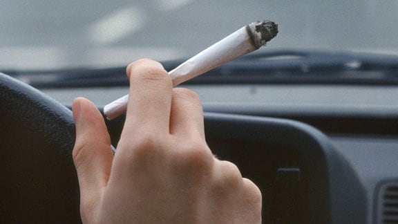 Ein junger Autofahrer raucht einen Joint waehrend der Autofahrt.