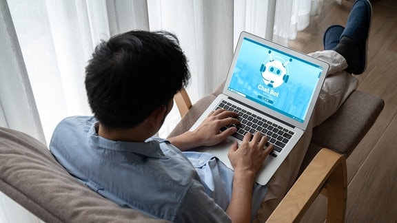 Mann kommuniziert an Laptop mit Chatbot