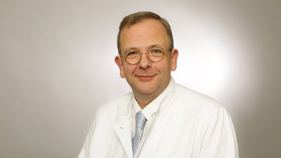 Poträtaufnahme eines Mannes mit Brille und im weißen Arztkittel. 