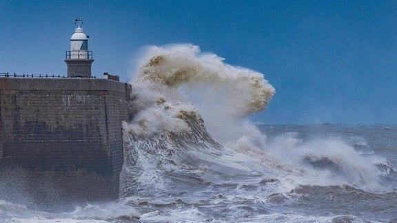 Stürmische Wellen Prallen auf eine Mauer auf der ein Turm steht.