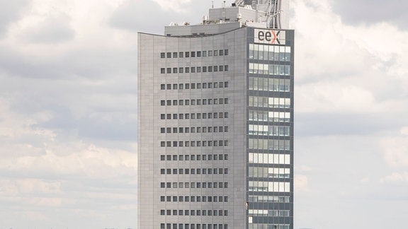 Grauer Wolkenkratzer mit kleinen Fenstern – City-Hochhaus – in 70er-Jahre-Stil in Stadtmitte von Leipzig, deutlich kleinere Gebäude in dichter Bebauung drum herum, Beschriftung "eex" an Hochhaus.