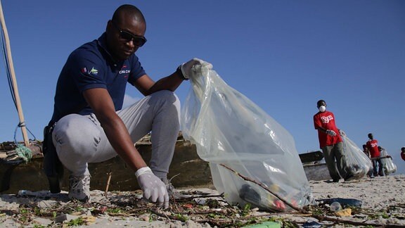 Menschen sammeln Müll vom Strand auf.