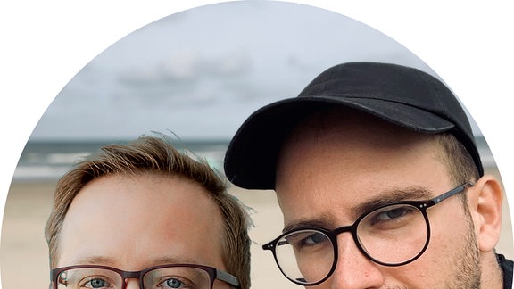 Fotomontage zwei junge Männer mit Brille, einer mit schwarzem Basecap, im Hintergrund Strand