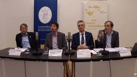 Eine Pressekonferenz, vier Männer an einem Tisch mit Mikrofonen