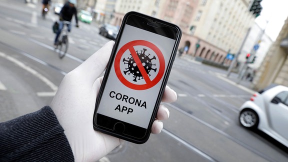 Bild eines durchgestrichenen Virus und Aufschrift Corona-App auf dem Display eines Smartphones