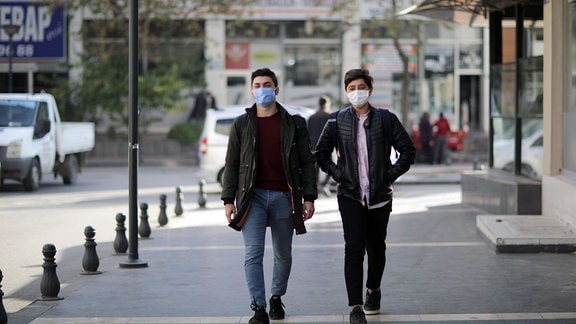 Zwei männliche Jugendliche mit Schutzmasken laufen auf einer Straße im südtürkischen Gaziantep, Frontalblick, Hintergrund leicht unscharf
