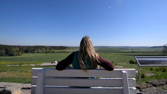 Eine Frau sitzt auf einer Bank unter blauem Himmel