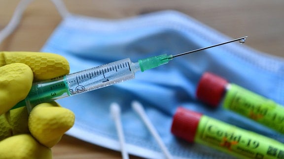 Eine Hand in Gummihandschuh hält eine Einwegspritze mit Impfstoff zur Injektion mit einer Kanüle.