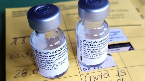 Zwei Impfdosen, Impfspritze und der Eintrag der ersten und zweiten Corona-Impfung in einem Impfpass