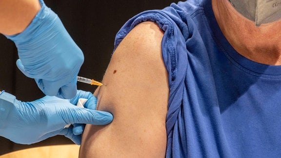 Ärztin setzt Impfspritze in den Oberarm eines älteren Mannes.