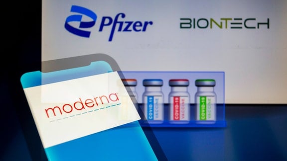 Moderna-Logo auf einem Smartphone, Pfizer- und BionTech-Logos im Hintergrund