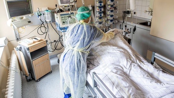 Eine Pflegerin versorgt eine im Koma liegende Frau im Patientenzimmer einer Coronastation.