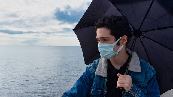 Ein junger Man mit Mundschutz und Regenschirm.