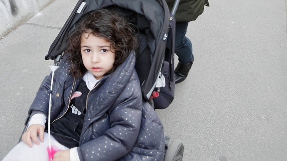 Passantin mit Mundschutz schiebt Kind im Kinderwagen