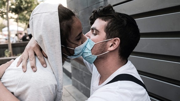 Ein junges Paar experimentiert damit, seine Zuneigung in der Öffentlichkeit mit obligatorischen Gesichtsmasken auszudrücken.