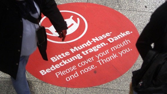 GroÃßer Aufkleber mit Piktogramm und Aufschrift Bitte Mund und Nase bedecken klebt auf dem Boden im Hauptbahnhof München