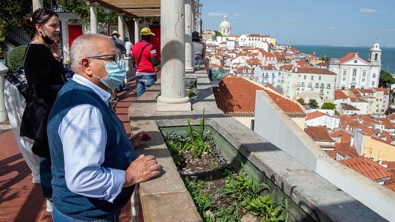 Ein Mann mit einer Schutzmaske blickt vom Aussichtspunkt Santa Catharina in Lissabon auf die Stadt.