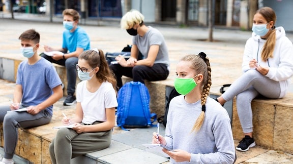 Porträt konzentrierter Teenager mit Gesichtsmasken während des Unterrichts vor der Hochschule an einem warmen Herbsttag.