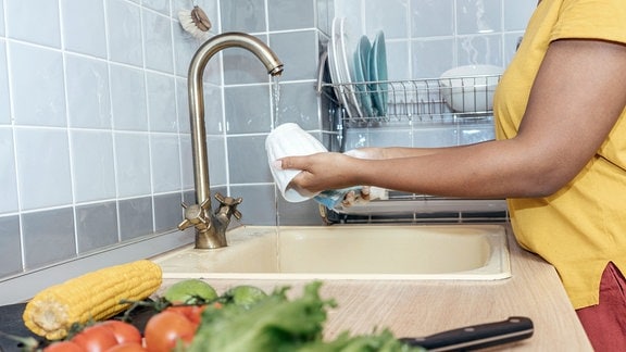 Eine Frau wäscht in der Küche Geschirr ab.