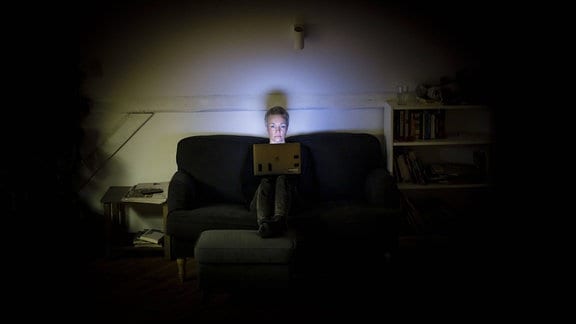Eine Frau sitzt nachts auf der Couch und schaut in ihren Laptop.
