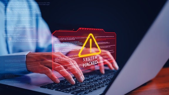 Foto/Grafik-Montage das die Hände einer Person an einem Laptop zeigt und darüber schwebend den Schriftzug "System Hacked"