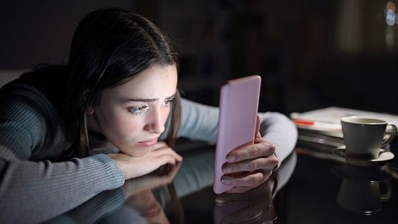 Eine junge Frau sieht traurig auf ihr Smartphone