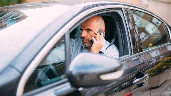 Geschäftsmann fährt Auto und nutzt Smartphone