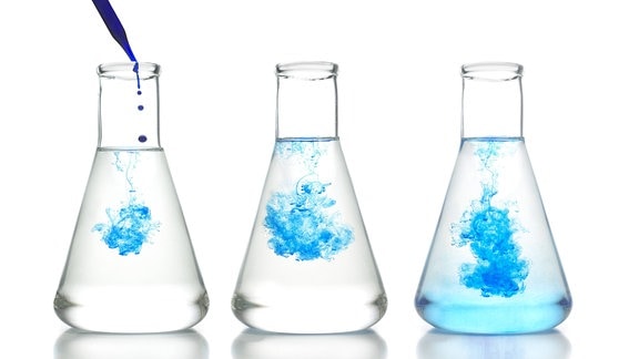 Eine blaue Flüssigkeit vermischt sich in einem Glaskolben mit Wasser.