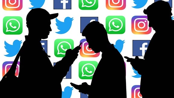 Silhouetten von Personen, die mit gesenktem Kopf auf den Bildschirm ihrer Smartphones schauen vor den Logos der sozialen Medien Instagram, Twitter, Facebook und Whatsapp