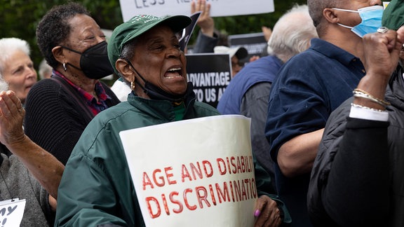 Eine Rentnerin in New York hält ein Schild mit er Aufschrift "Age and Disability Discrimination"