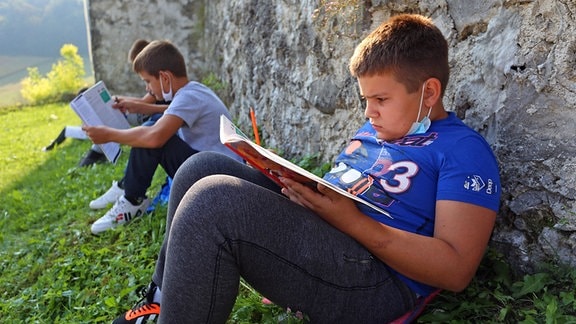 Kinder einer sechsten Klasse sitzzen im Outdoor-Unterricht auf einer Wiese