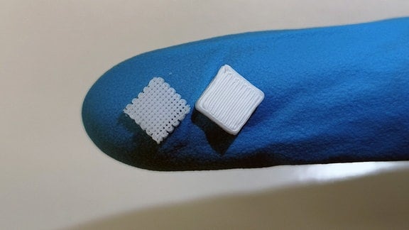 Zwei kleine 3-D-Objekte liegen auf Fingerspitze in Handschuh
