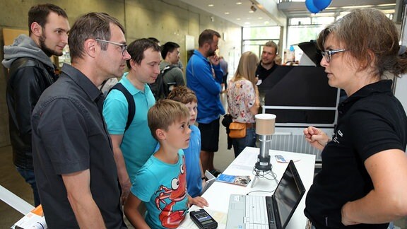 Eine Frau an einem Stand spricht mit Besuchern.