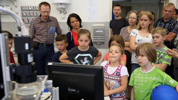 Kinder und Erwachsene schauen einen Computerbildschirm an.